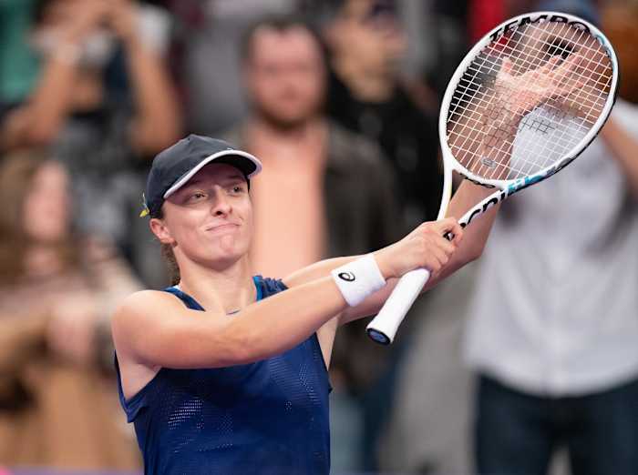 Iga Swiatek claps, hand against tennis racket, after winning a match
